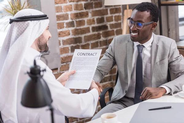 Un homme d'affaires arabe sous contrat et serrant la main d'un partenaire afro-américain — Photo de stock