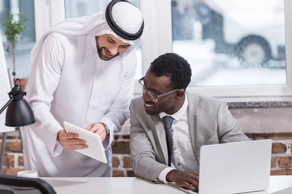 Arabian businessman showing digital tablet to african american partner in office — Stock Photo