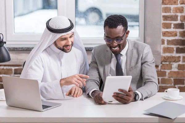 Des hommes d'affaires multiculturels regardant la tablette numérique dans un bureau moderne — Photo de stock