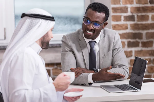 Afrikanisch-amerikanischer Geschäftsmann zeigt arabischem Geschäftspartner Laptop — Stockfoto