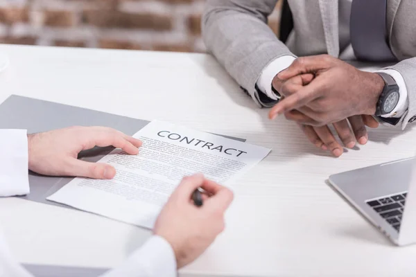 Vista recortada de empresarios multiétnicos firmando contrato en la oficina moderna - foto de stock