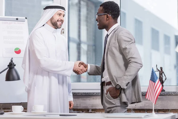 Alegre hombres de negocios estrechando la mano y sonriendo en la oficina - foto de stock
