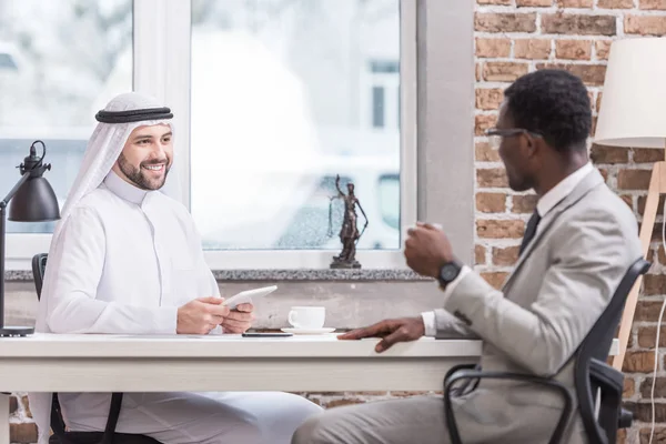 Homme d'affaires arabe tenant une tablette numérique et ayant une réunion avec un partenaire afro-américain au bureau — Photo de stock
