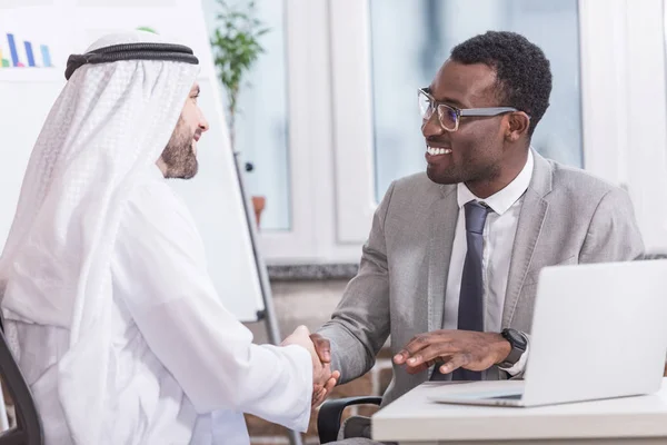 Gli uomini d'affari multiculturali sorridenti che stringono la mano in ufficio moderno — Foto stock
