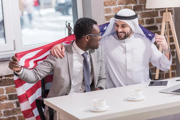 Des hommes d'affaires multiethniques tenant le drapeau américain dans un bureau moderne — Photo de stock