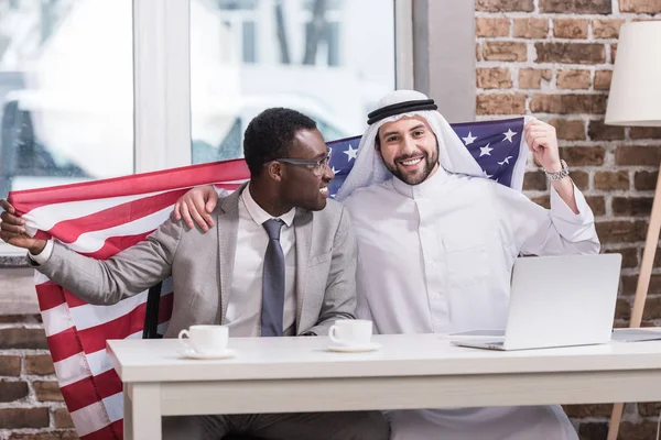 Des hommes d'affaires multiculturels tenant le drapeau américain dans un bureau moderne — Photo de stock