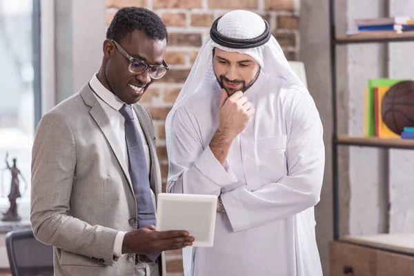 Arabe homme d'affaires regardant tablette numérique et la pensée près partenaire afro-américain — Photo de stock