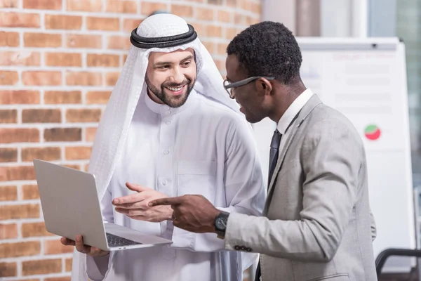 Empresarios multiculturales señalando a la computadora portátil en la oficina moderna - foto de stock