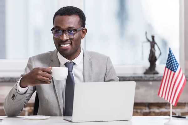 African american businessman holding cup with drink in modern office — Stock Photo