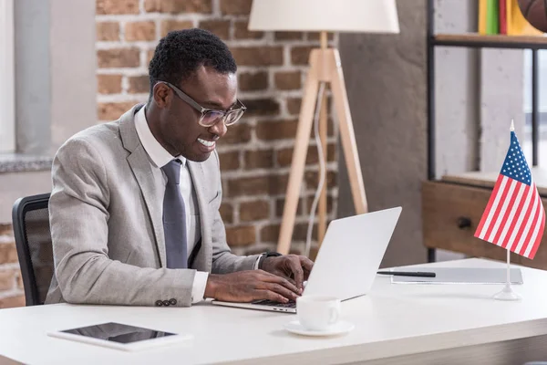 African american businessman sitting at office desk and using laptop — Stock Photo