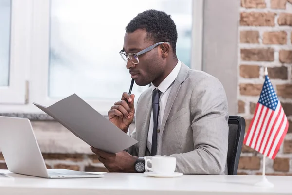 African american businessman holding folder and sitting at office desk — Stock Photo