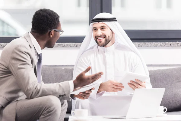 Multicultural businessmen having discussion and holding gagets in office — Stock Photo