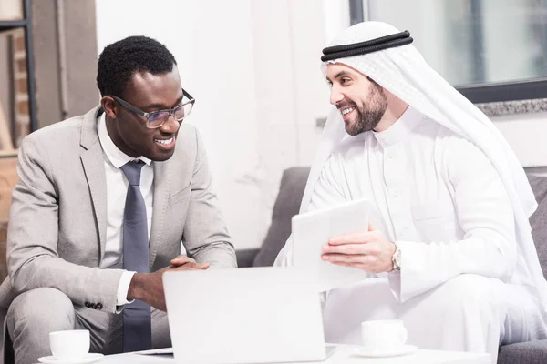 Hombre de negocios árabe mostrando tableta digital a socio afroamericano en la oficina - foto de stock
