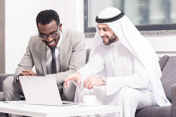 Arabe homme d'affaires à la recherche d'un ordinateur portable avec un partenaire afro-américain au bureau — Photo de stock