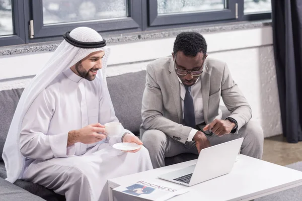 Багатокультурні бізнесмени сидять і дивляться на ноутбук в сучасному офісі — стокове фото