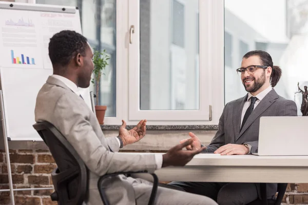 Handsome multiethnic business partners sitting at office desk — Stock Photo