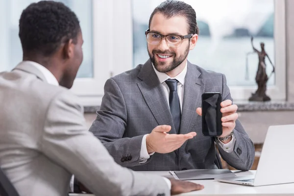 Smiling businessman showing smartphone screen to african american partner in office — Stock Photo