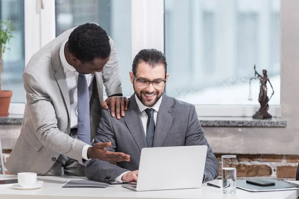 Hombre de negocios afroamericano poniendo la mano en los socios hombro y apuntando a la computadora portátil en la oficina - foto de stock
