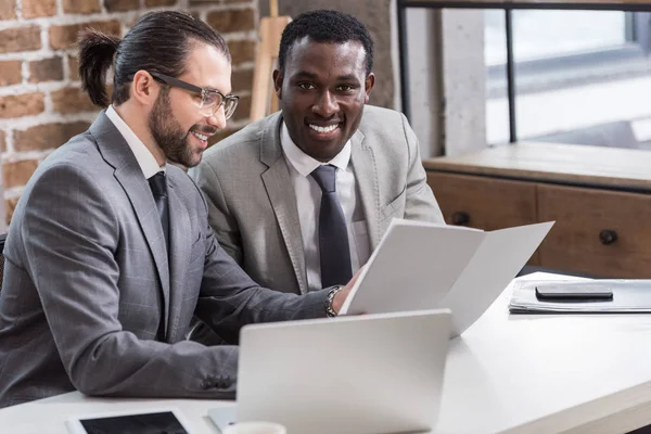 Schöner Geschäftsmann liest Dokument, während afrikanischer amerikanischer Partner im Büro in die Kamera schaut — Stockfoto