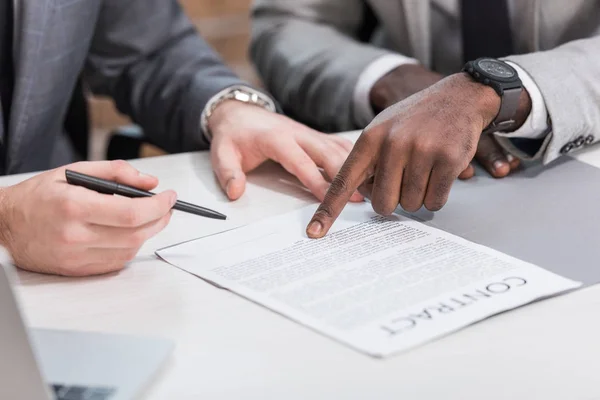 Обрезанный взгляд многонациональных деловых партнеров на подписание контракта на офисном столе — стоковое фото