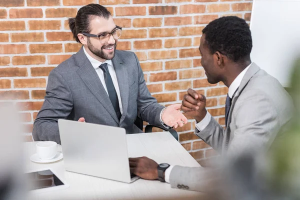 Multiethnische Geschäftsleute lächeln und unterhalten sich am Tisch mit Laptop — Stockfoto