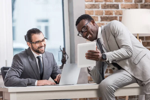 Partenaires d'affaires multiethniques souriant et regardant la tablette numérique au bureau — Photo de stock