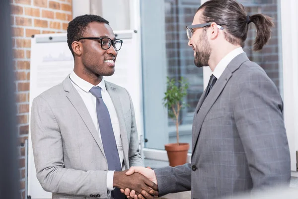 Smiling multiethnic businessmen shaking hands in office — Stock Photo