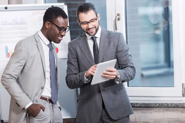 Multiethnische Geschäftspartner stehen im Büro und schauen auf digitales Tablet — Stockfoto