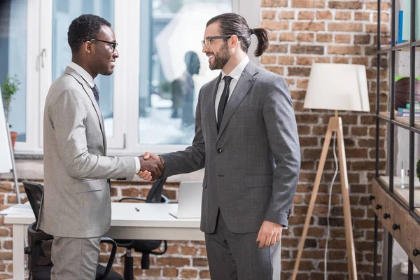 Smiling multiethnic business partners shaking hands in modern office — Stock Photo