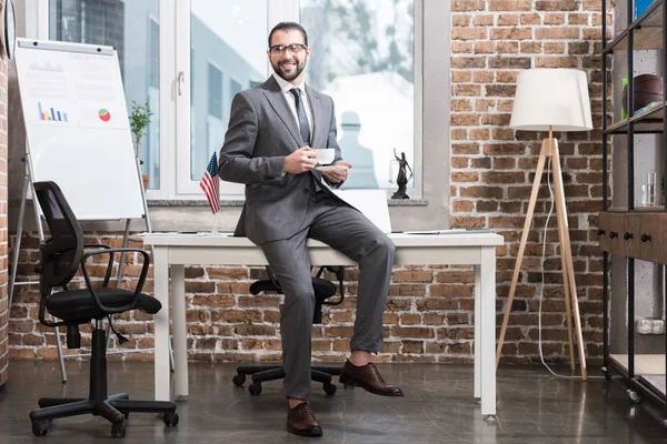 Красивый бизнесмен сидит за столом и держит чашку кофе в офисе — стоковое фото