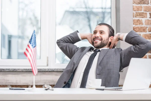 Успешный бизнесмен с руками на голове сидя за столом офиса — стоковое фото