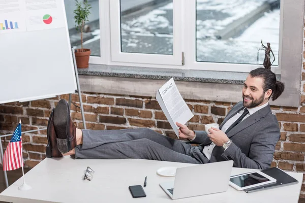 Sorridente empresário sentado à mesa e colocando os pés no escritório — Fotografia de Stock