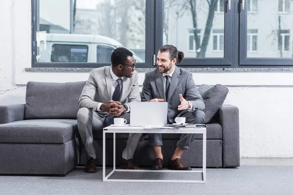 Socios empresariales multiétnicos sentados en el sofá y debatiendo - foto de stock