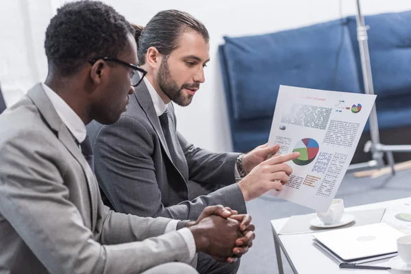 Multiethnic business partners looking at document with charts in office — Stock Photo
