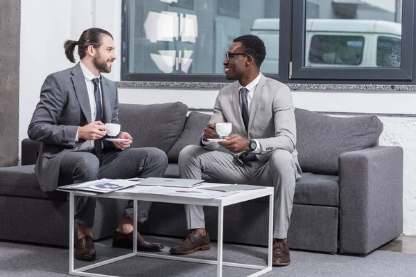 Multiethnische Geschäftsleute sitzen auf der Couch und trinken Kaffee im Büro — Stockfoto