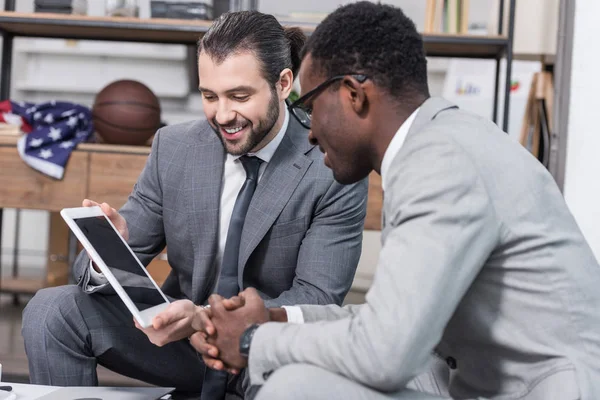Bell'uomo d'affari che mostra lo schermo del tablet digitale al partner commerciale afro-americano in ufficio — Foto stock