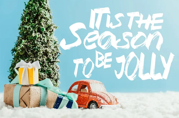 Close-up shot of toy red car with presents and christmas tree standing on snow made of cotton on blue background with 