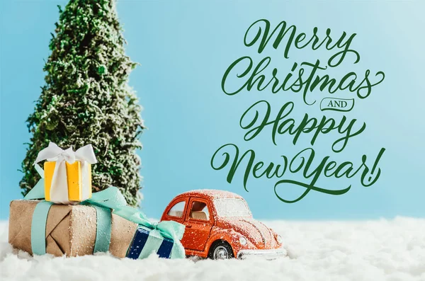 Close-up shot of toy red car with presents and christmas tree standing on snow made of cotton on blue background with 