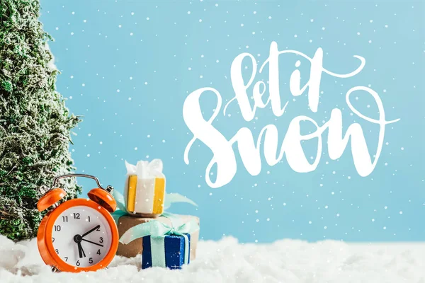 Close-up shot of christmas gifts with alarm clock and miniature christmas tree standing on snow on blue background with 