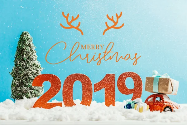 Большие красные номера 2019 года с игрушечной машиной, подарками и елкой на снегу с надписью 