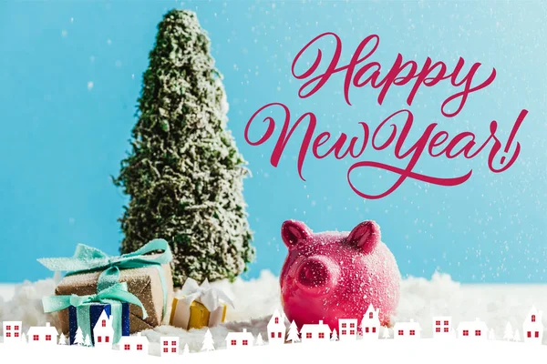 Miniature christmas tree with gifts and piggy bank standing on snow on blue background with 