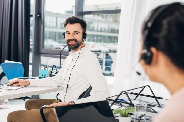Handsome call center operator smiling and looking to colleague in office — Stock Photo