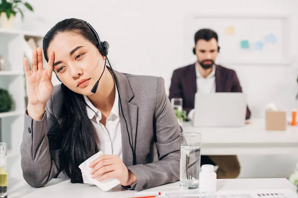 Sick call center operator touching head and holding napkin in office — Stock Photo