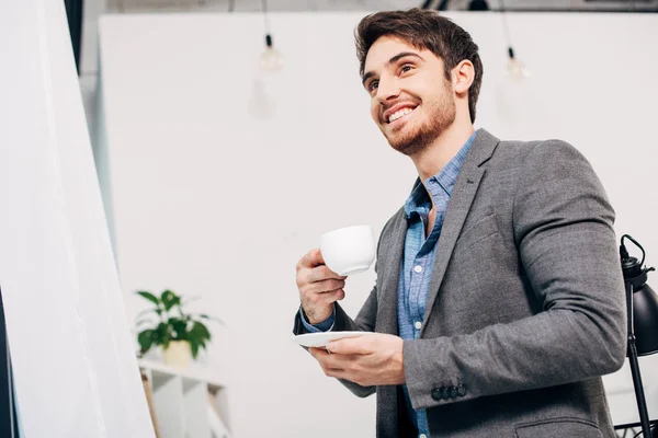 Handsome office manager smiling and holding coffee cup in office — Stock Photo