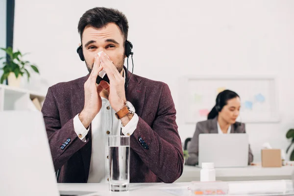 Sick call center operator with napkin blowing nose in office — Stock Photo