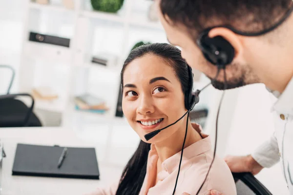 Operador atractivo centro de llamadas sonriendo y mirando a colega en la oficina - foto de stock