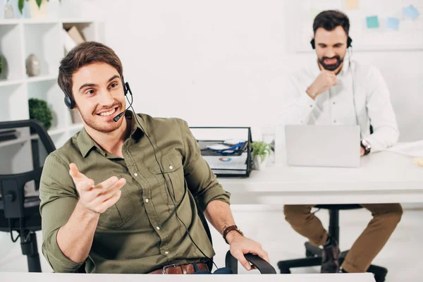 Operador de call center bonito com fone de ouvido sorrindo e falando no escritório — Fotografia de Stock