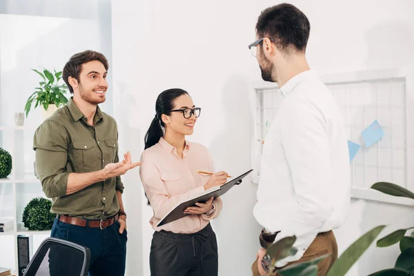 Zufriedene Büroleiter, die mit Post-Notizen vor der Tafel stehen und im Büro reden — Stockfoto