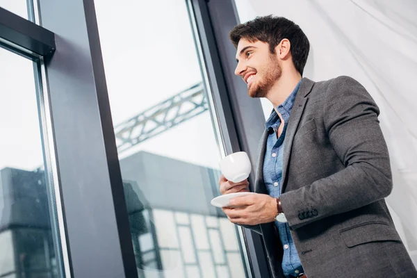 Young businessman holding cup of coffee and looking in window — Stock Photo
