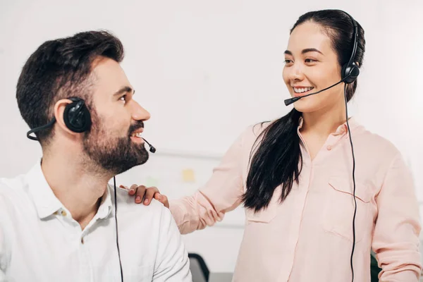 Primer plano de la gestora poniendo la mano en la tijera de compañero de trabajo masculino en auriculares en la oficina - foto de stock